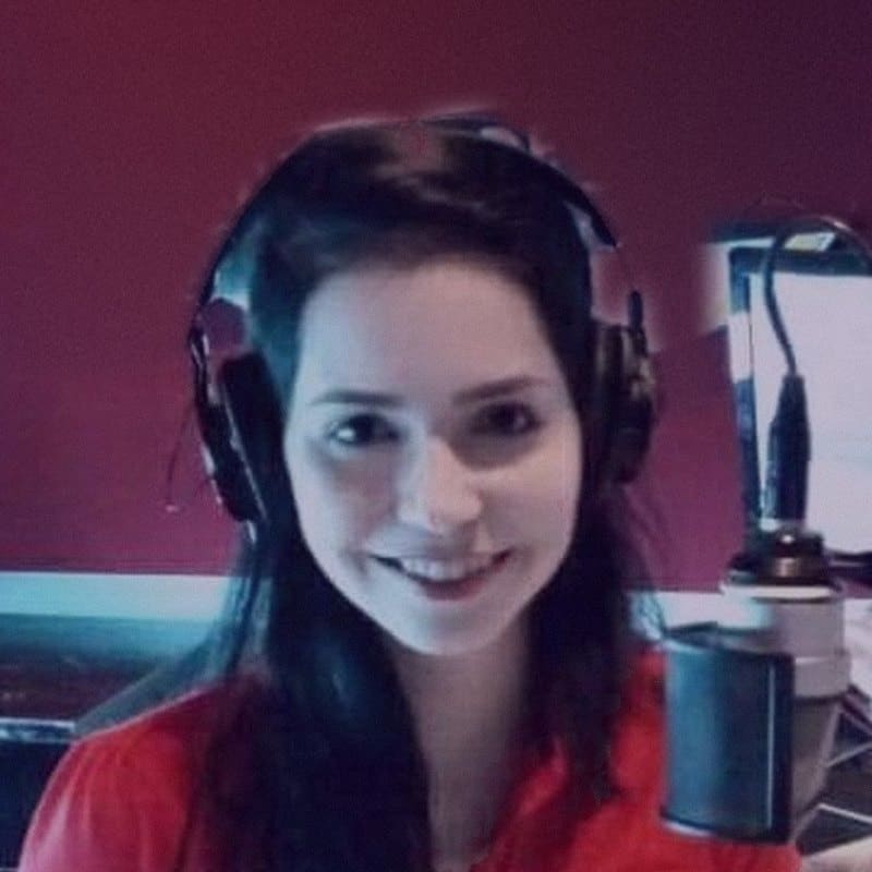 Flávia Sandroni de fones de ouvido, sorrindo diante do microfone num estúdio de rádio.